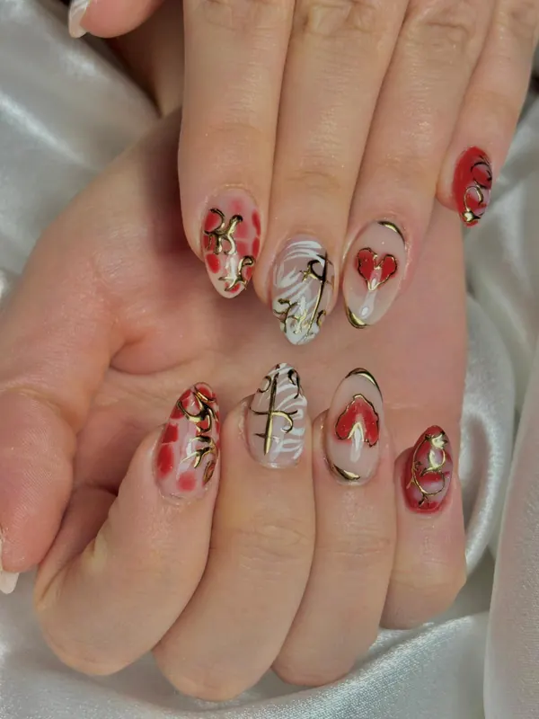 Uñas nude con corazones rojos y detalles dorados en relieve